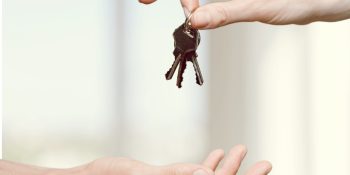 Apartment. Hand giving set of house keys on blurred background